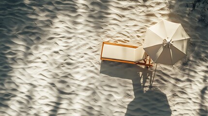 An overhead view of a chaise lounge and umbrella set on an empty, sunlit beach. The lounge chair leaves imprints in the soft sand, and the shadow of the umbrella adds contrast to the scene.