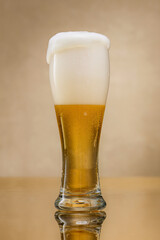 Beer. Overflowing craft beer on a golden, yellow  background with reflection. Glass of fresh and cold beer.  Shallow depth of field