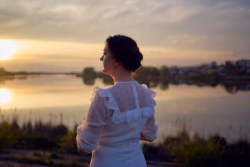 a woman in a white vintage dress on the shore of a lake at sunset