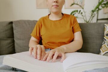 Unrecognizable woman with disability enjoying reading Braille book while sitting on comfortable...