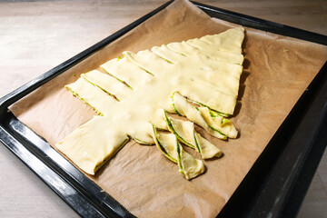 Puff pastry dough filled with homemade green pesto is cut in a Christmas tree on a baking tray, creative recipe for a holiday party, copy space, selected focus