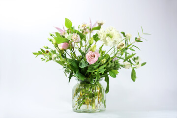 Bouquet of delicate flowers with white and soft pink blossoms in a glass vase against a light gray background, copy space, selected focus