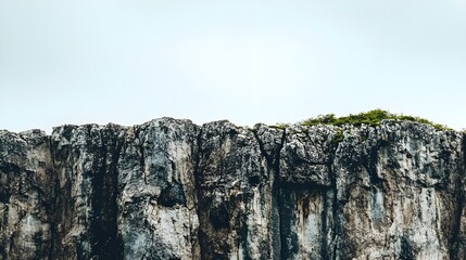 A rugged cliff with patches of green vegetation under a cloudy sky, showcasing the beauty of nature's landscapes.