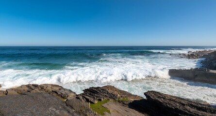 Waves crashing against a rocky coastline, with white foam spreading over the beach
