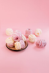 Pink and white marshmallows on a plate with a sprinkle of powdered sugar on a pink background. Meringue. Marshmallow.