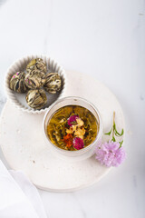 Green asian Tea in a glass with a blooming large flower. Teapot with exotic green tea-balls blooms flower on light grey background. Tea ceremony. Vertical top view