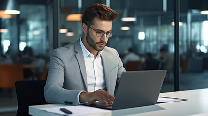 Fototapeta premium A young businessman is working diligently on his laptop in a modern office.