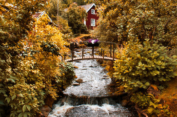 Stream with a small bridge in front of a red wooden house in Sweden in autumn.