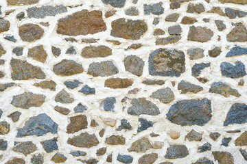 Background of a natural stone or sandstone masonry wall with cement in South France. Detailed stone texture image in beige, brown, grey and blue	