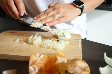 Close up of female hands cutting raw onions on wooden board, blurry background 