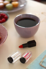 Plate of pastel macarons, cookies and chocolate, cup of tea of coffee, glass of bubble water, various berries, books and accessories on the table. Selective focus, pastel colors.