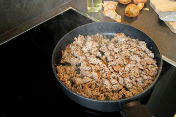 Close up cooked ground beef meat frying in a pan in the kitchen, blurry background with onions and oil spray 