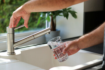 Close up of male hands pouring tap water into a glass in the kitchen