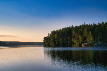 Fototapeta premium Lake in Sweden at sunrise with romantic light, blue water and trees on the shore