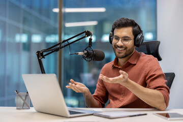 Podcast host engagingly speaks into microphone wearing headphones. In modern office setting, laptop...