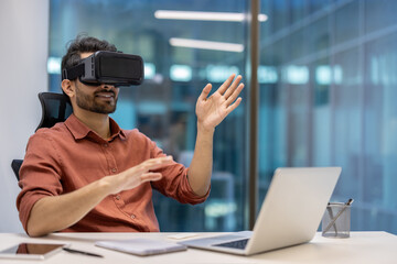 Man using VR headset immersed in virtual reality seated at office desk. Hands engaged in interaction with digital content. Modern workplace environment showcasing technology innovation and engagement