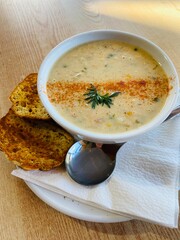 A Bowl of salmon chowder served with toasted bread on the white plate on the wooden table 