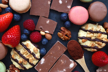 Macarons, chocolate, cookies, berries and various nuts on dark blue background. Top view.