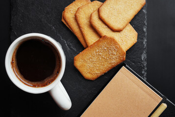 Cup of coffee next to cinnamon sugar cookies and notepad with pen on dark background