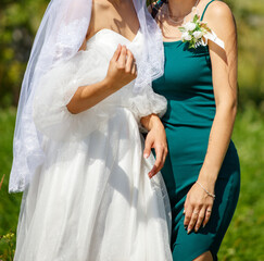 Bride in a wedding dress and bridesmaid outdoors in summer. Detailed photo