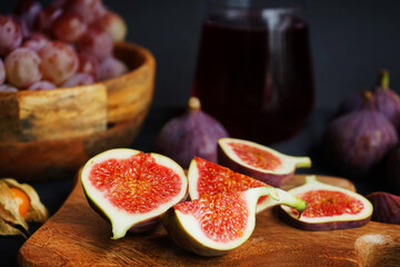 Ripe whole and sliced ​​figs with Physalis fruits, pink grapes on a wooden board and a glass of red wine on a dark background