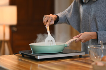Cropped shot of young woman cooking with frying pan on stovetop in cozy kitchen