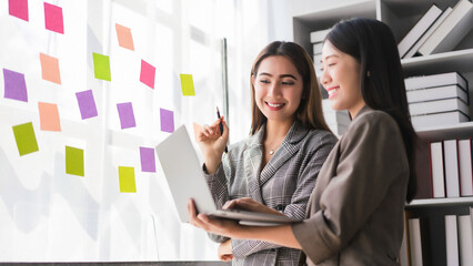 Two businesswoman reading business data on laptop and writing strategy ideas in sticky notes