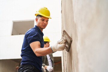 Young male mason with trowel applying cement on wall at construction site