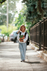 Holding notepad. Schoolgirl with backpack is outdoors