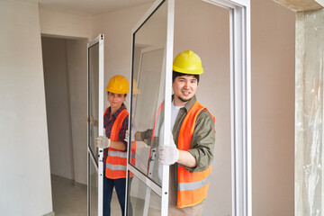 Portrait of smiling male and female carpenters carrying window frames at incomplete house site