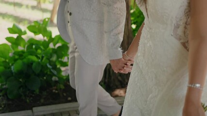 bride and groom in elegant attire walking hand in hand outdoors, enjoying a peaceful moment together
