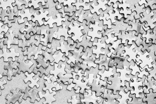 A close-up shot of scattered puzzle pieces in black and white. The pieces are arranged randomly, creating a sense of chaos and incompleteness