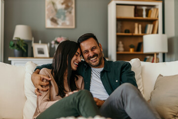 Loving modern couple sitting on the sofa, man holding a remote controller and watching a TV together