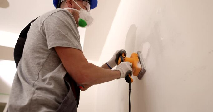 Craftsman sands gray plastered wall with special manual machine with emery net. Repairman removing putty defects in the process of finishing work