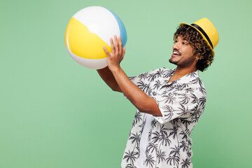Side view young cool Indian man wear beach shirt hat rest near hotel pool hold in hand inflatable...