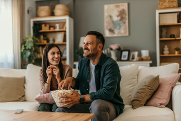Loving couple at home, spending the relaxed day together. They are watching TV and eating popcorns
