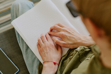 Pale hands of unrecognizable man with disability on snow white page with dots, top down shot