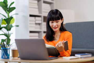 Focused young asian businesswoman write in notebook, learning, using laptop. Concept of remote work, studying with computer
