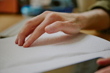 Medium close up of unrecognizable male hand touching embossed paper of Braille book