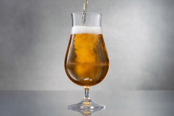 Beer. Glass of fresh and cold beer.  Stream of draught beer in glass. Glass of fresh and cold light beer on a gray background with reflection.  Shallow depth of field