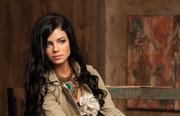 Fototapeta premium Beautiful brunette woman posing in art studio. Young lady with long curly hair and make-up on brown background indoor