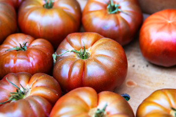 Closeup of  fresh vibrant red,  green heirloom tomatoes in a carton cardboard box at local farmers market. Assorted organic heirloom beef tomatoes. Healthy eating, gardening, and farm-to-table concept