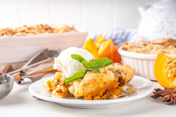 Homemade autumn pumpkin crisp cobbler, pumpkin crumble pie with crunchy dough topping in baking dish and plate, with ice cream scoop on white kitchen table