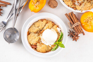 Homemade autumn pumpkin crisp cobbler, pumpkin crumble pie with crunchy dough topping in baking dish and plate, with ice cream scoop on white kitchen table