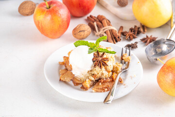 Apple Crumble Dessert, crisp cobbler with Ice Cream, crumble pie with crunchy dough topping in baking dish and plate, with ice cream scoop on white kitchen table