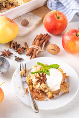 Apple Crumble Dessert, crisp cobbler with Ice Cream, crumble pie with crunchy dough topping in baking dish and plate, with ice cream scoop on white kitchen table