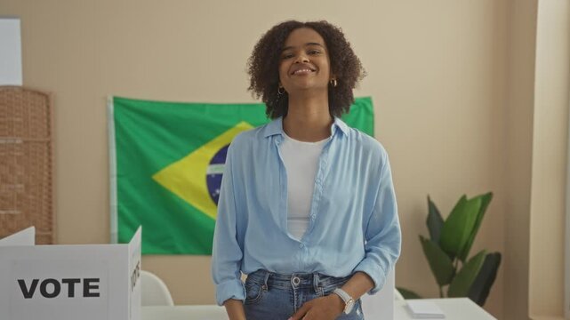 Young african american woman with curly hair points to the camera while standing in an electoral college room with brazilian flag and vote sign background.