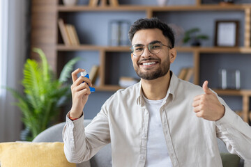 Smiling man using inhaler in home setting gives thumbs up showing relief and comfort