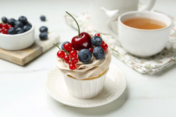 Tasty cupcake with different berries and tea on white marble table