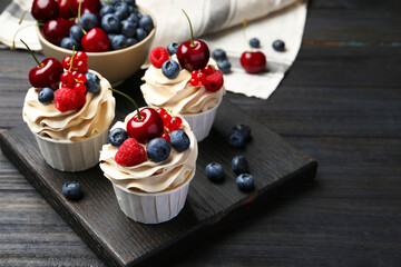 Tasty cupcakes with different berries on black wooden table, space for text